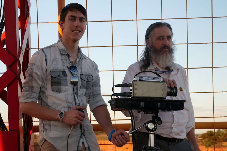 Daniel Jensen and Richard Sonnenfeld stand at a lookout, holding a camera on a tripod.