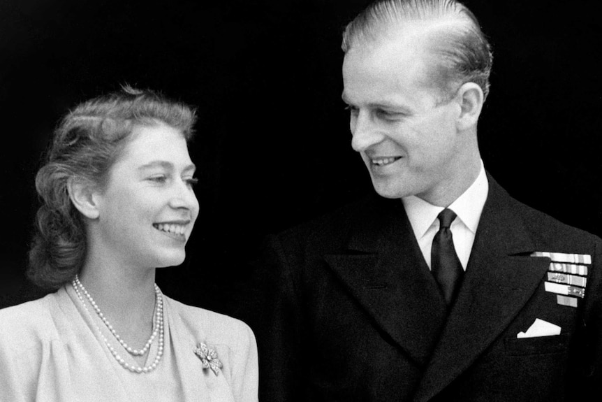 A black and white photo of Princess Elizabeth and Philip Mountbatten smiling as they stand side by side.