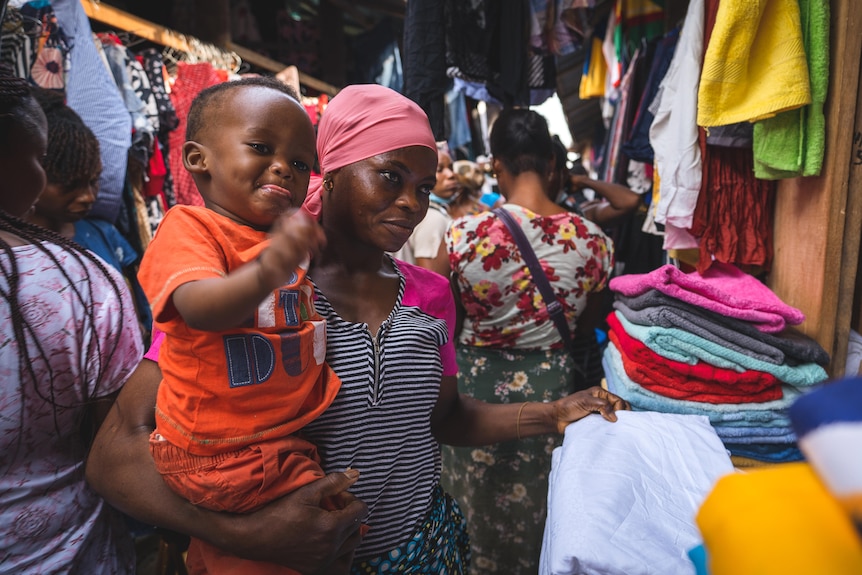 A woman holds her son in a clothing market.
