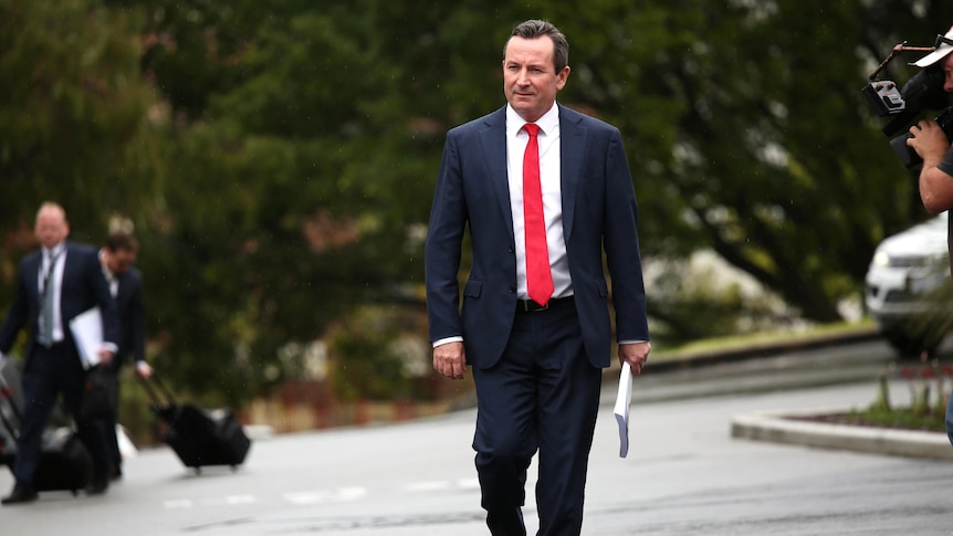 A wide shot of Mark McGowan walking wearing a red tie.