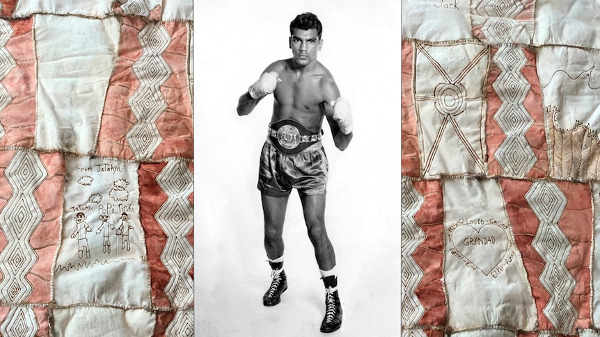 Black and white photo of a boxer in satin shorts, with fists raised between two patchwork panels of ochre and white fabric.