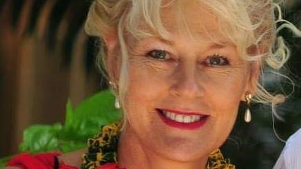 A middle-aged woman with blonde curly hair and pearl earrings smiles broadly.