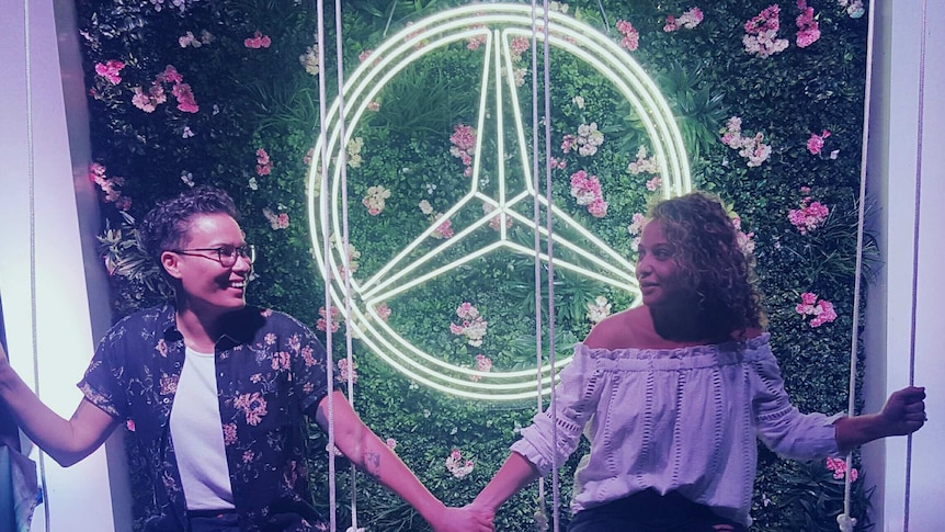 Nathalie Lagrasse and Nicole Domonji hold hands as they sit on a swing.