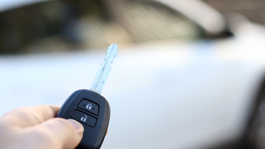 A car key in front of a car out of focus in the background.