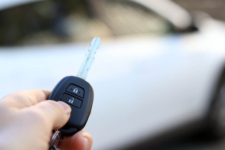 A car key in front of a car out of focus in the background.