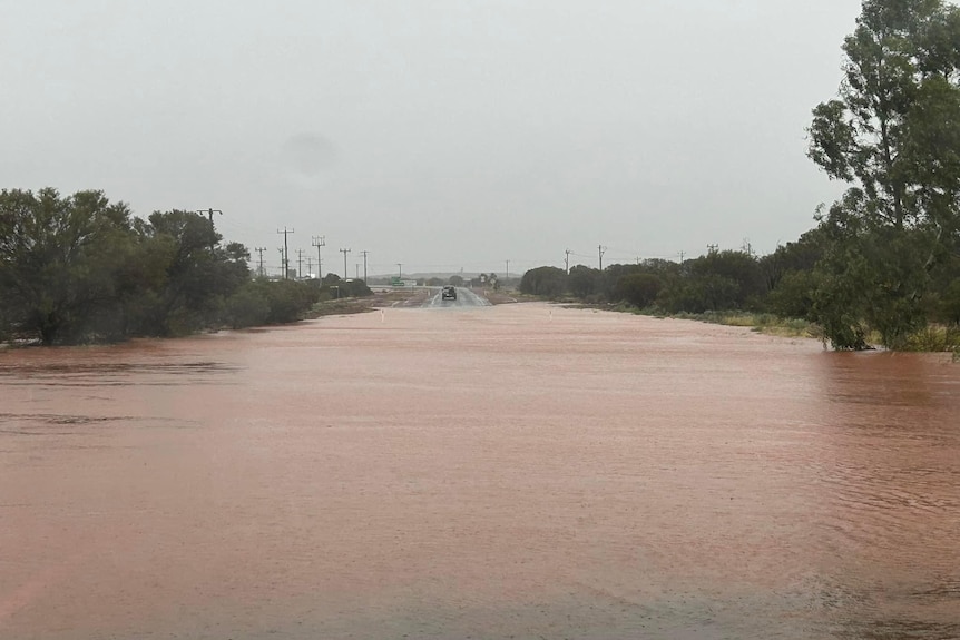 Inondation d'une route de l'arrière-pays avec une voiture au loin.   