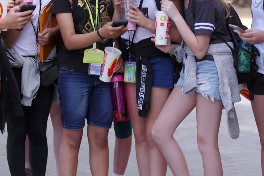 a group of young girls standing around and using their mobile phones, you can only see their legs