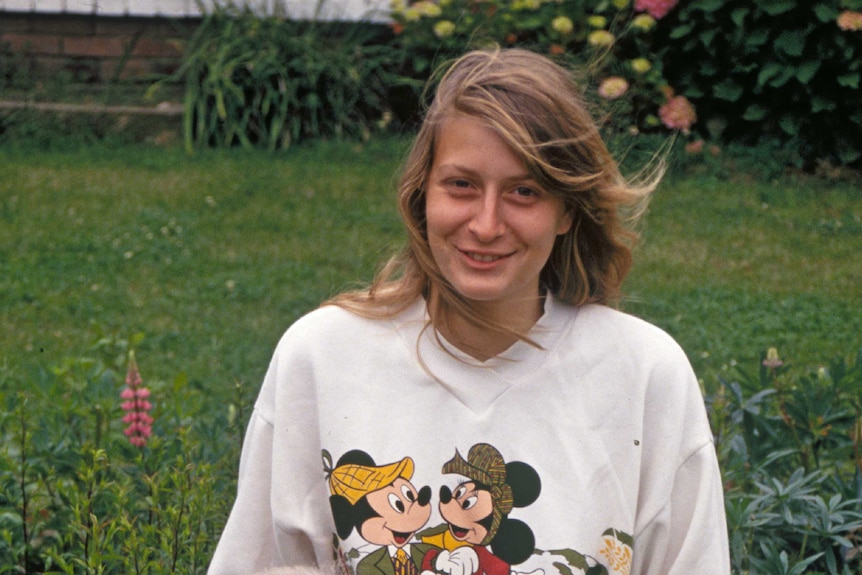 A young, smiling blonde woman in a garden.