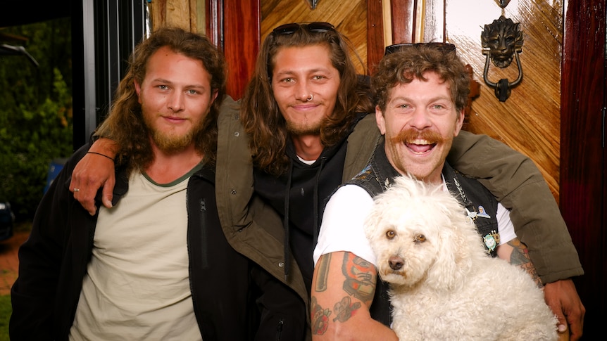 The three men smile with their arms over each other's shoulders.