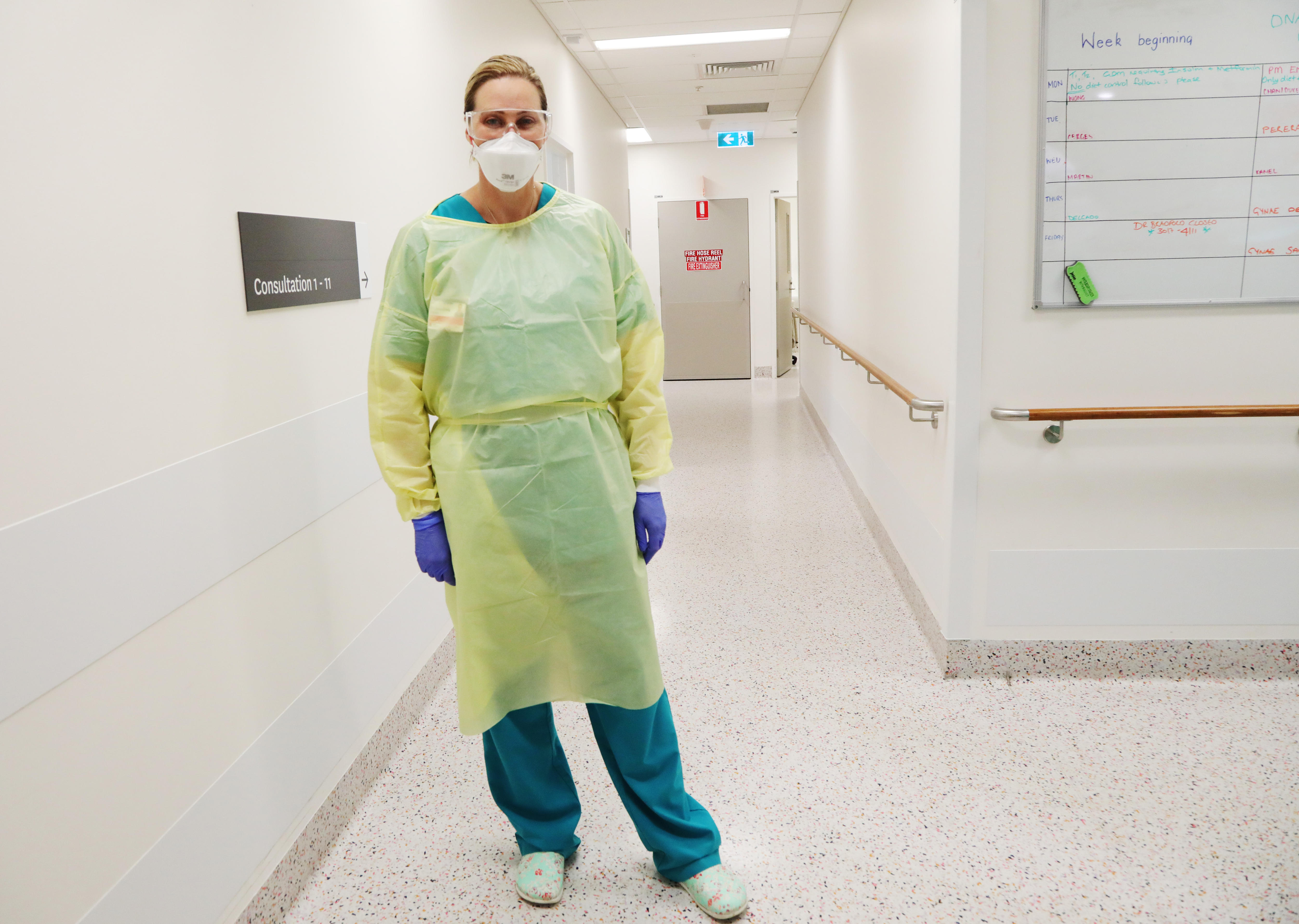 A female doctor in full PPE stands in a ward hallway