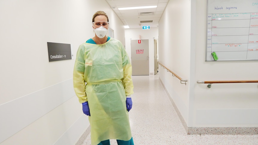 A female doctor in full PPE stands in a ward hallway