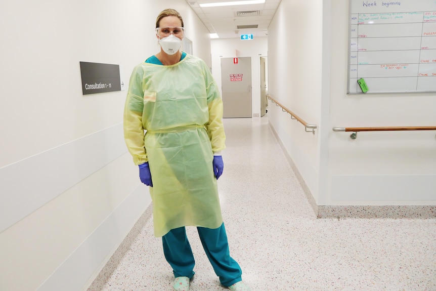 A female doctor in full PPE stands in a ward hallway