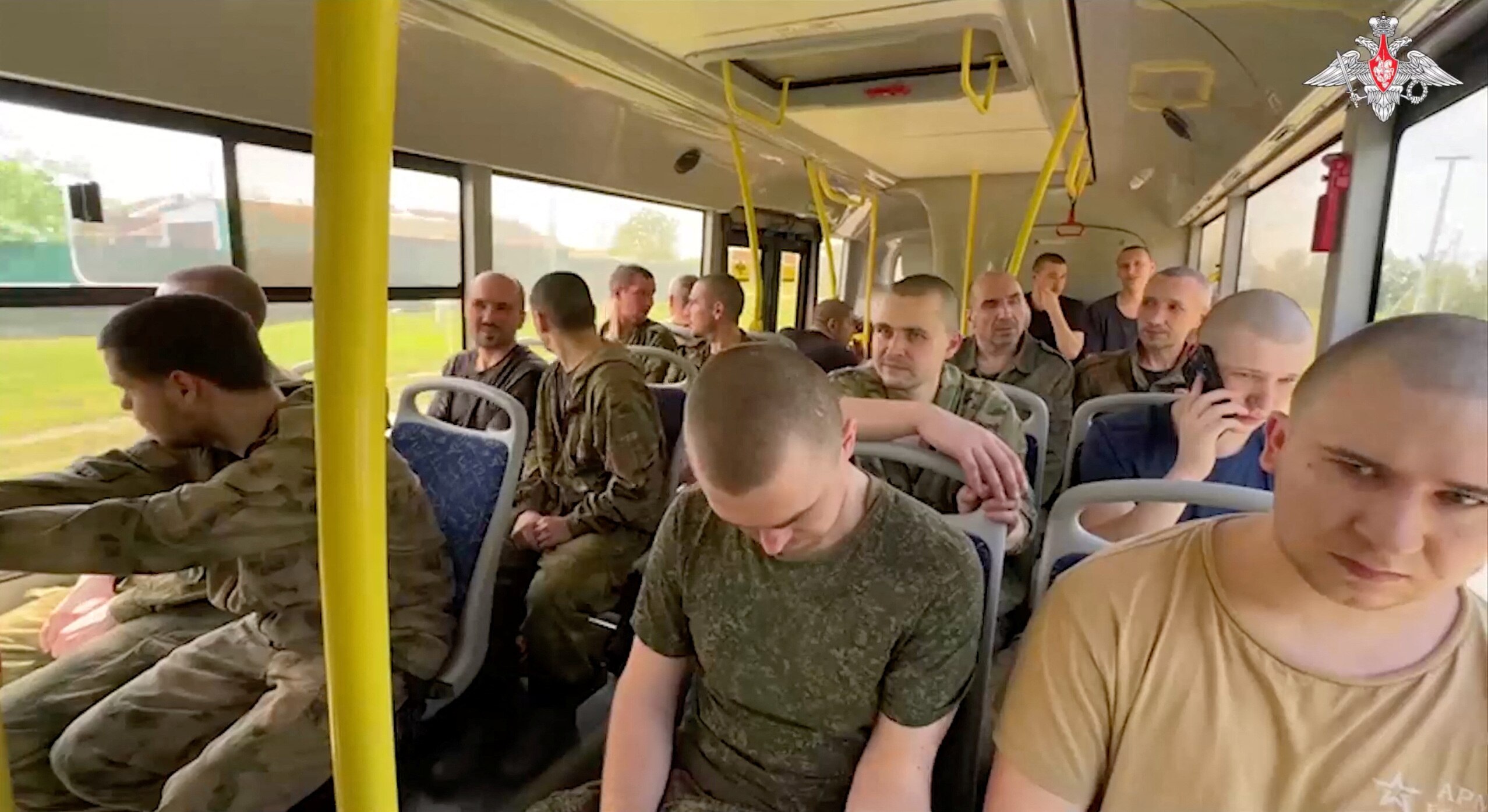 Men with shaved heads sit in military coloured clothing on a bus