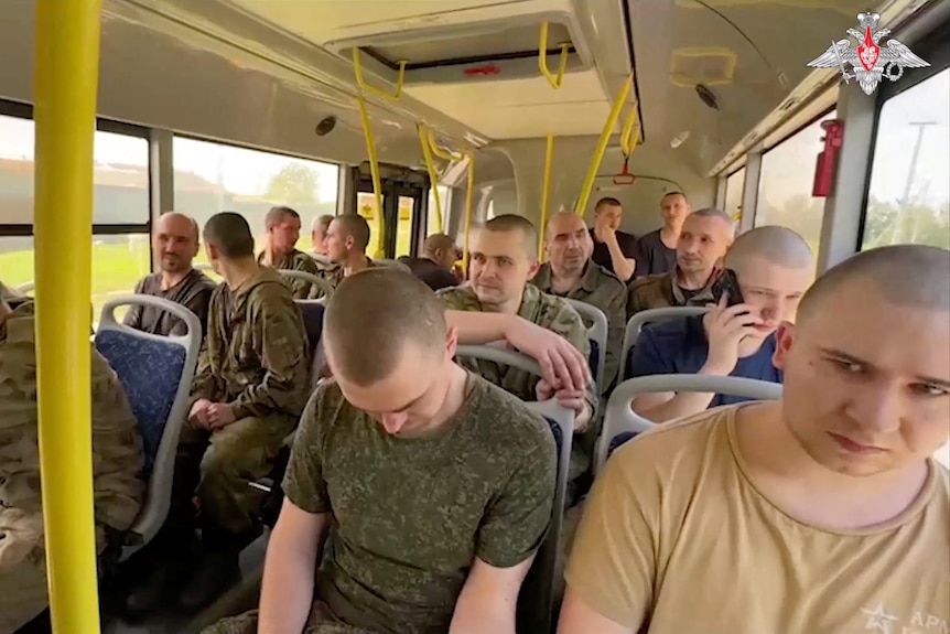 Men with shaved heads sit in military coloured clothing on a bus