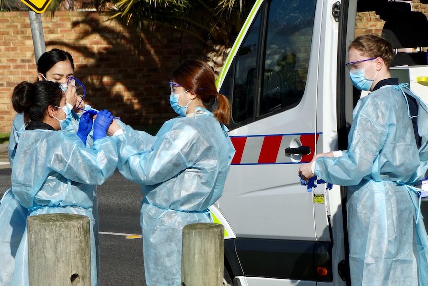 A group of women wearing blue PPE gear and wearing masks stand in the street.