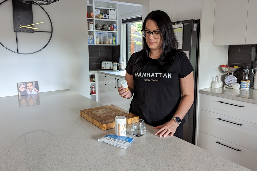 A young white woman with long dark hair looking at a bottle of medication