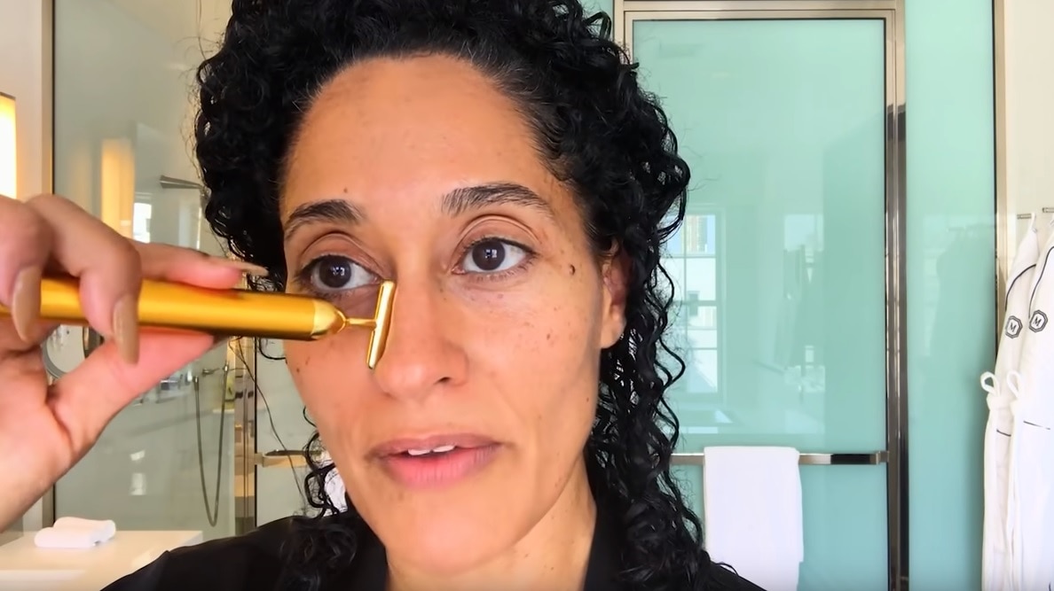 Woman in bathroom places small face massager on her face