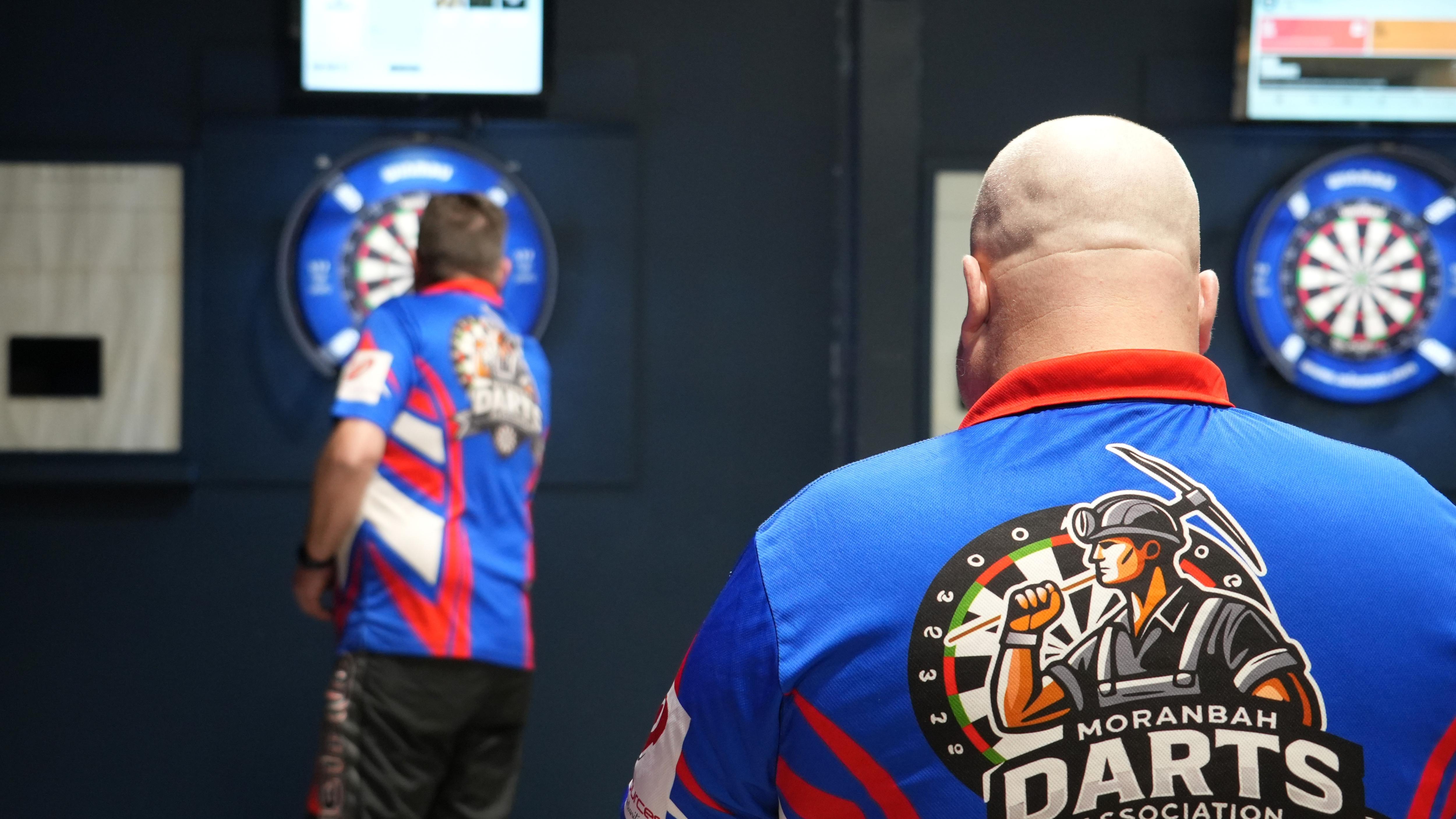 Back of darts shirt with graphic, man in foreground at board 