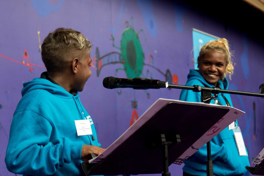 Two kids smile at each other shyly on stage