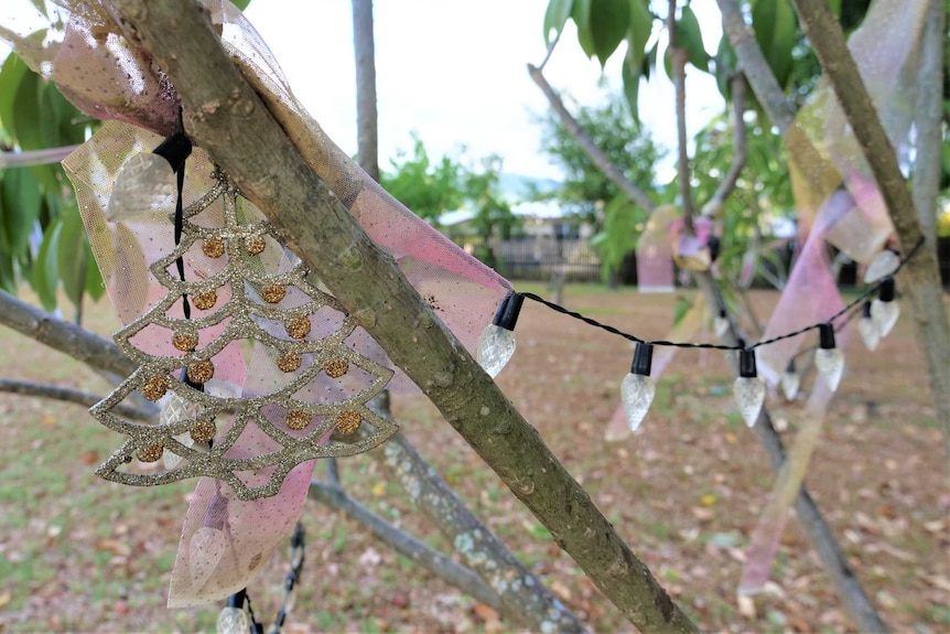 Close-up of sparkly Christmas tree decoration and  string of lights on branches of a frangipani tree