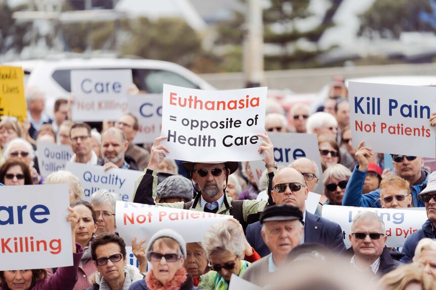 A crowd of people holding up placards protest at a rally outside WA Parliament House against voluntary euthanasia.