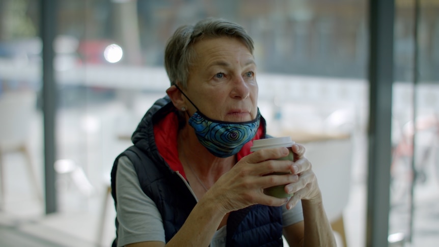 A woman sits, staring off into the distance, holding a cup of coffee