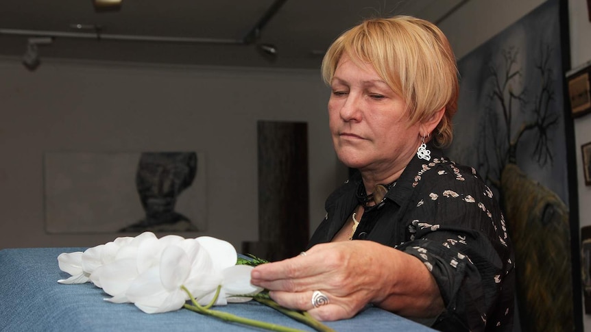 Small business owner Carol Phayer looking over a cardboard casket adorned with fake flowers.