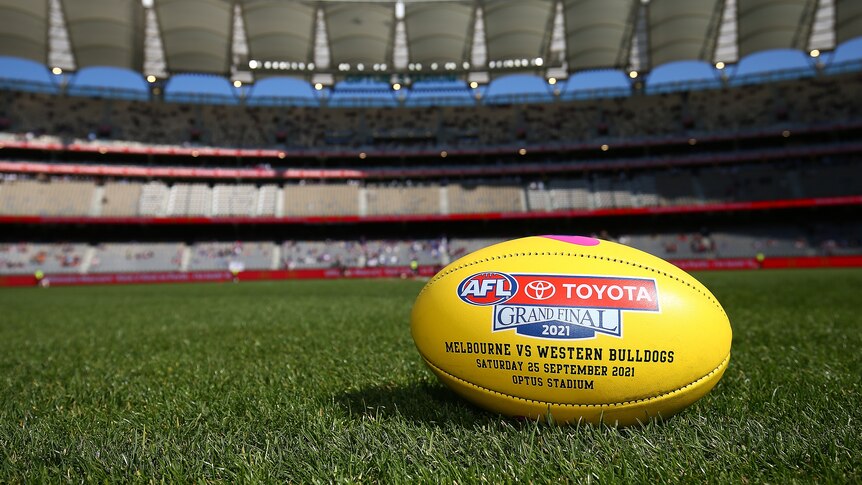 A close-up of an AFL football lying on the grass in an empty stadium. 
