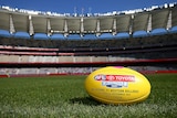 A close-up of an AFL football lying on the grass in an empty stadium. 
