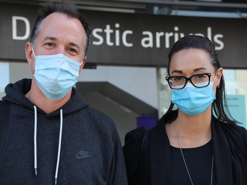 A man and a woman wearing masks outside the airport.