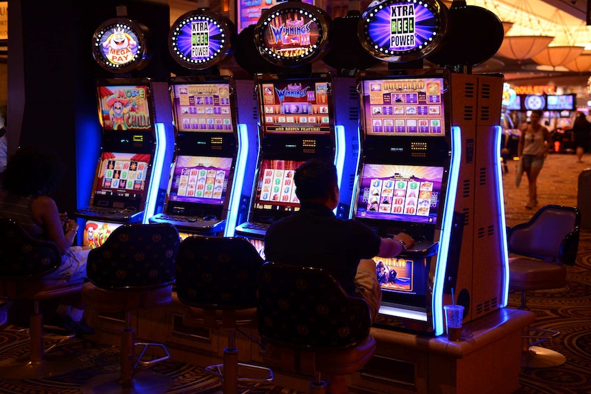 A close-up of bright poker machine in a casino and two people sitting in front.