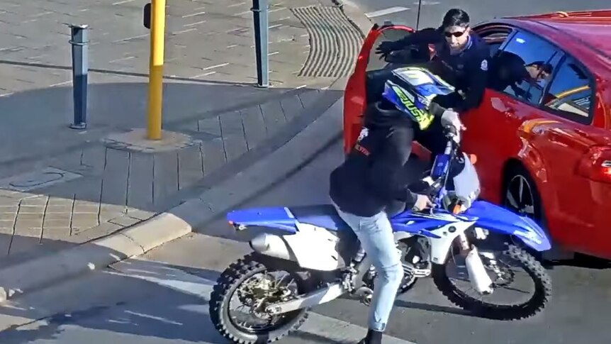 A policeman leaps the passenger side of an unmarked car as a motorcycle rider tries to escape.
