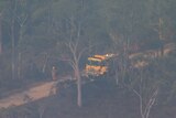 an aerial photo of a firefighter standing next to a yellow fire truck assessing a grass fire in thick bushland