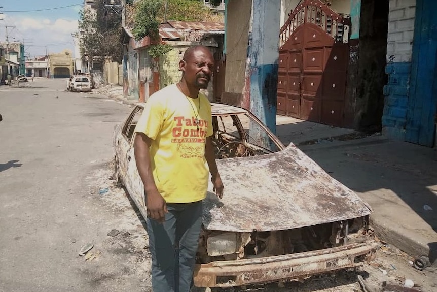 Pierre Ricot stands next to his burnt out car in Port-au-Prince, Haiti