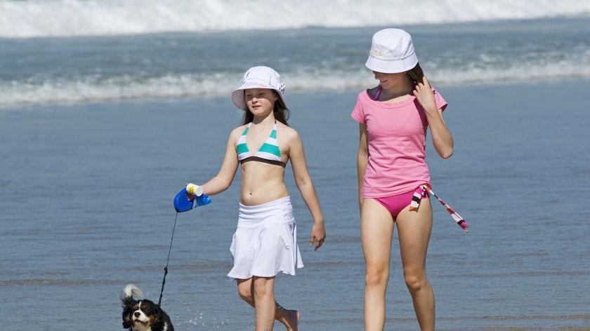 two girls walking on along a beach with a dog on a lead