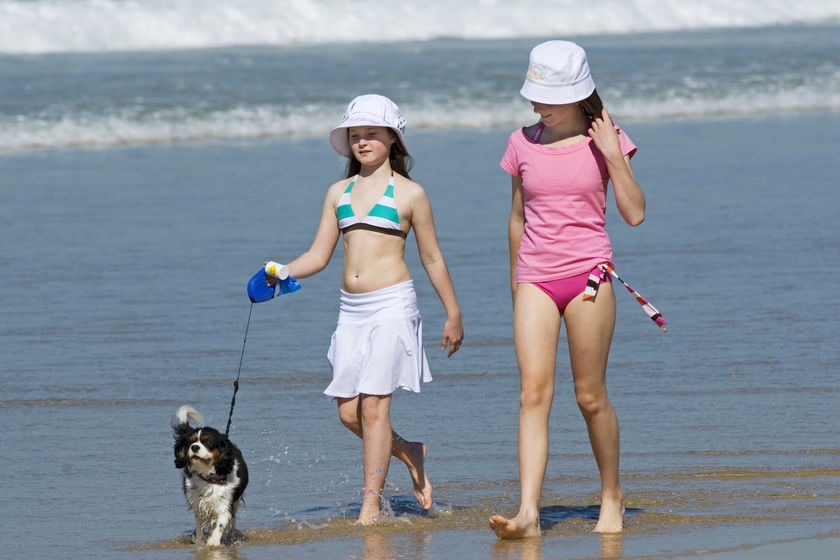 two girls walking on along a beach with a dog on a lead