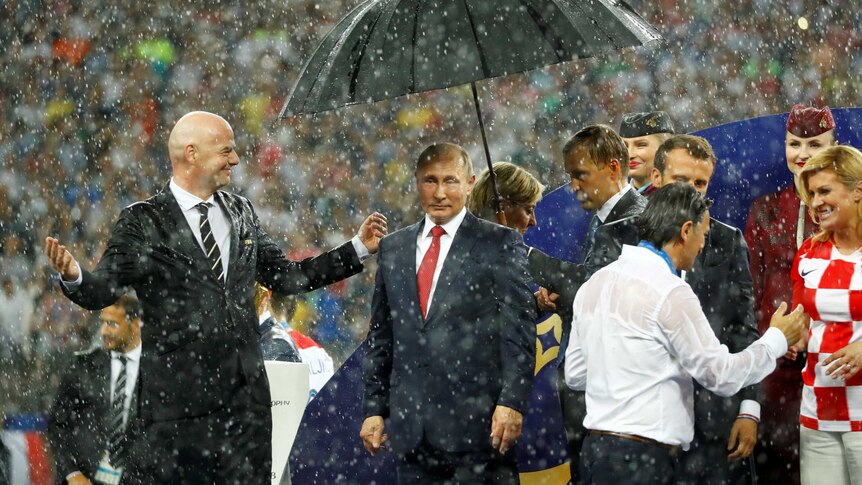 Putin stands under an umbrella amid heavy rainfall on the field