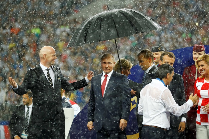 Putin stands under an umbrella amid heavy rainfall on the field