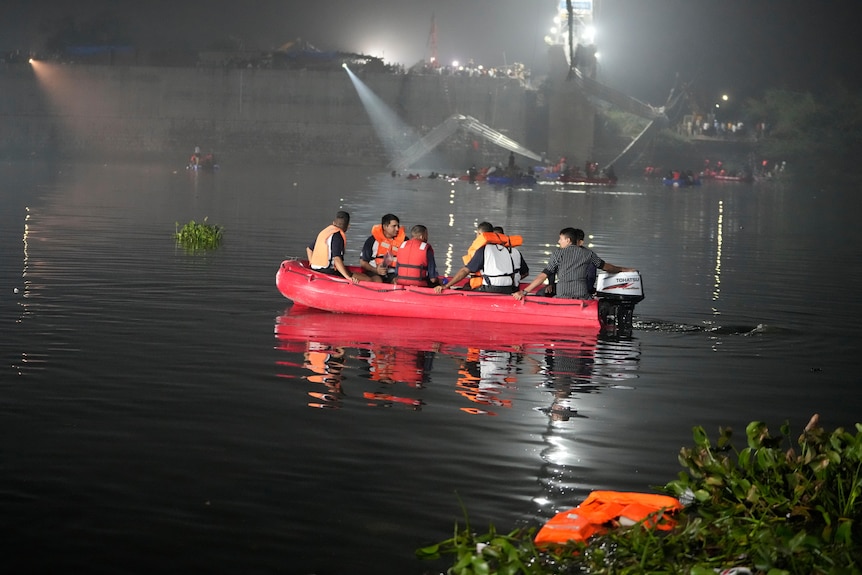 A red dinghy with five people in life jackets crosses the water at night time