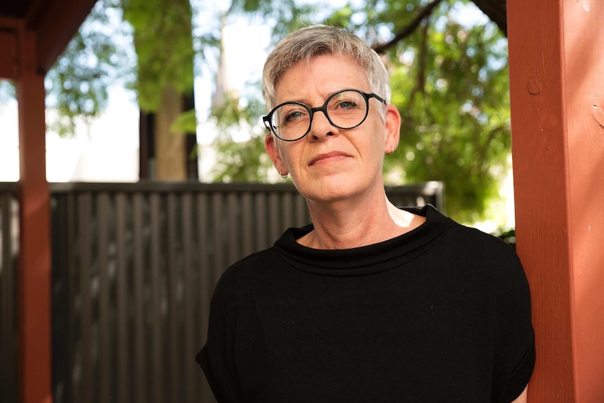 A woman looks at the camera with a backyard fence in the background.