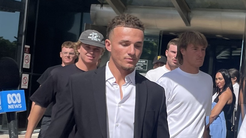 A man in a suit walks with young men around him outside a court.
