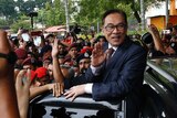Anwar Ibrahim stands outside a car and waves as a crowd of photographers and police surround him.
