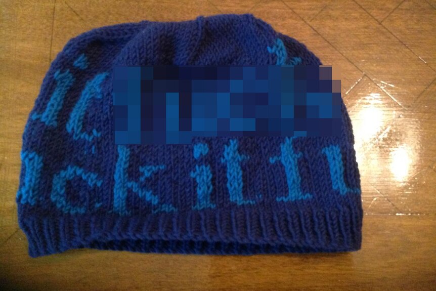 An image of a beanie with text of an expletive knitted into it.