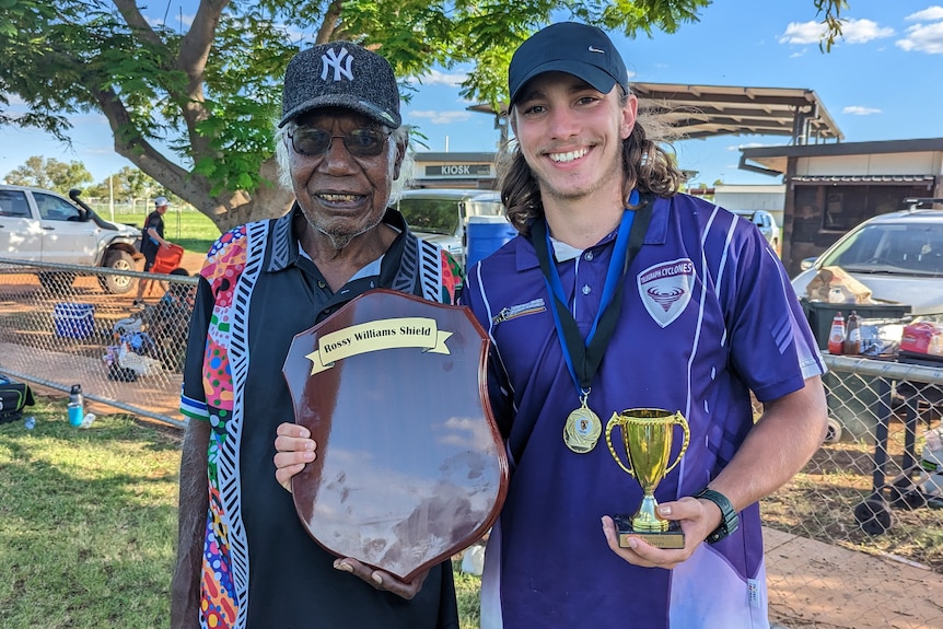 Two men stand together pleased at the Purkiss sporting reserve in Tennant Creek, Lachie holds a shield and tropy.