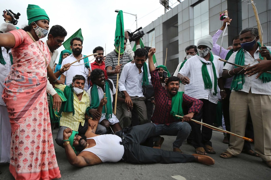 A farmer lies on the road and shouts slogans during a protest against new farming laws in Bangalore