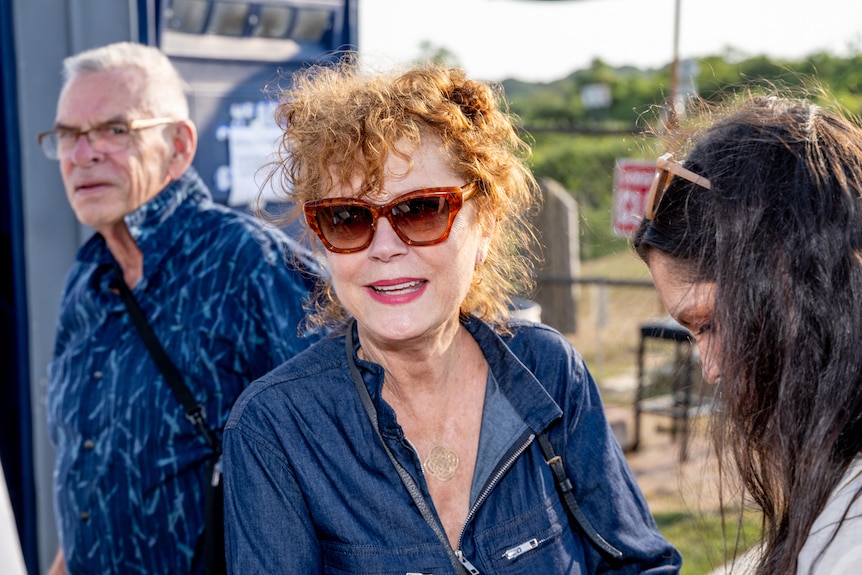 Actress Susan Sarandon smiles as she wears red sunglasses and a blue shirt
