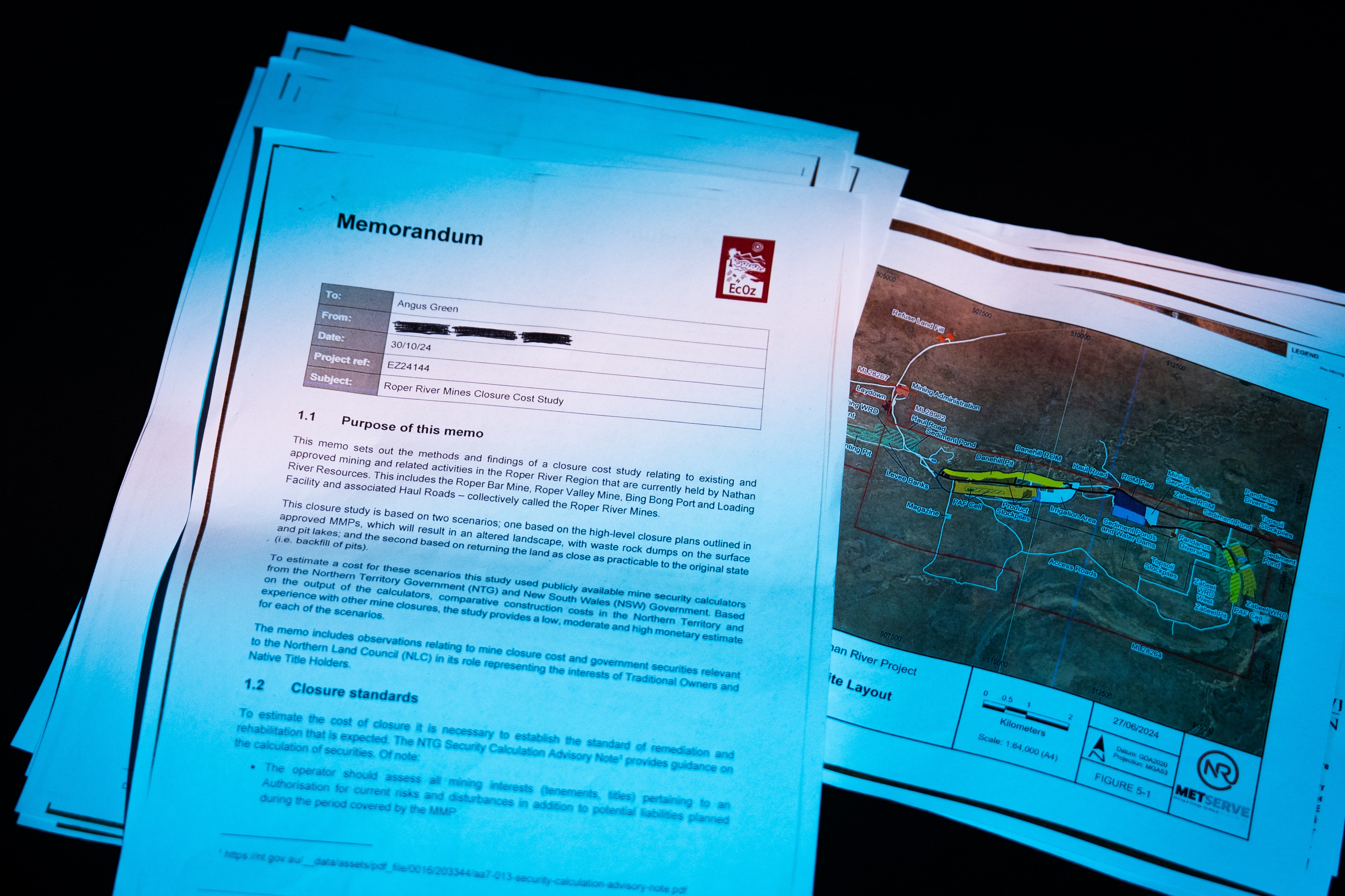 Birds-eye-view of report documents spread out, including a map of an area of land, on a black background.