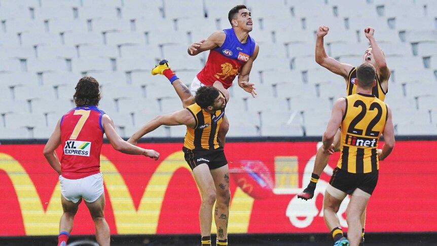 An AFL player launches on the shoulders of another player trying to mark in front of an empty stand.