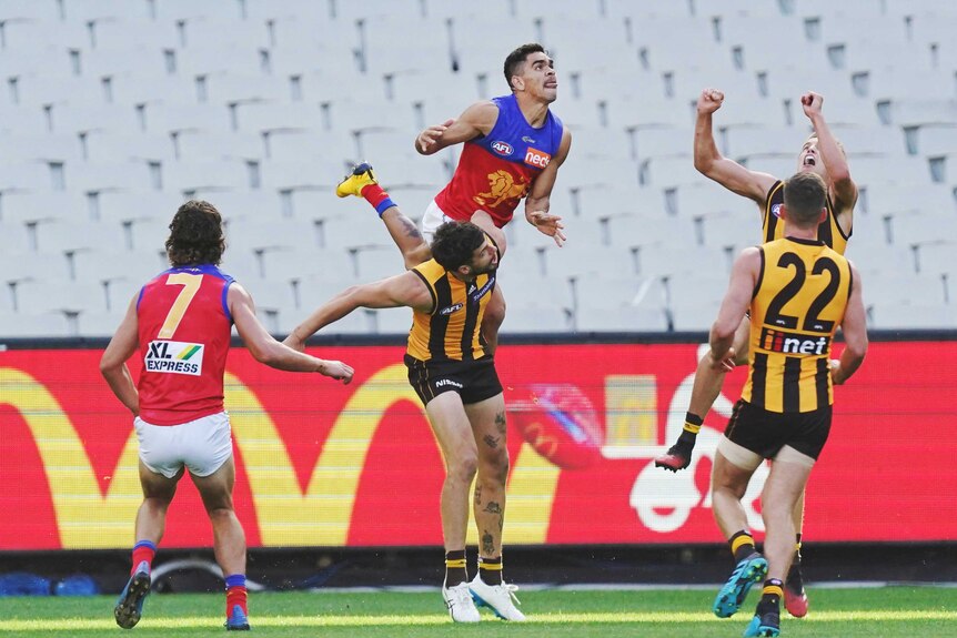An AFL player launches on the shoulders of another player trying to mark in front of an empty stand.