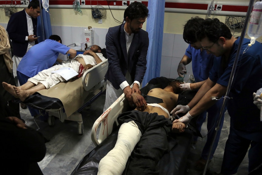 Men in bandages lie in hospital as doctors treat them.